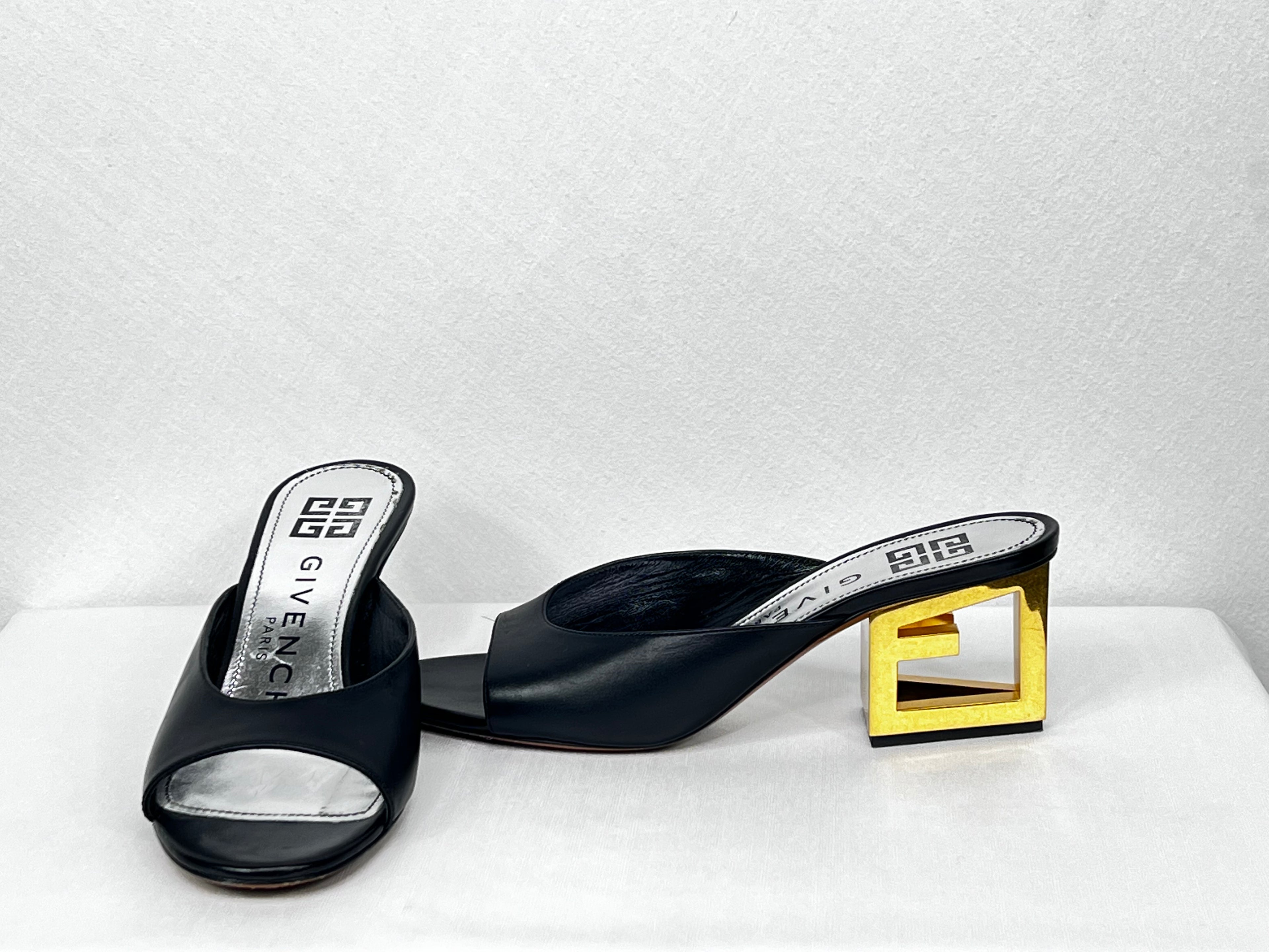 Pre-owned Givenchy black leather open-toe mules featuring sculptural gold block heel, angled view