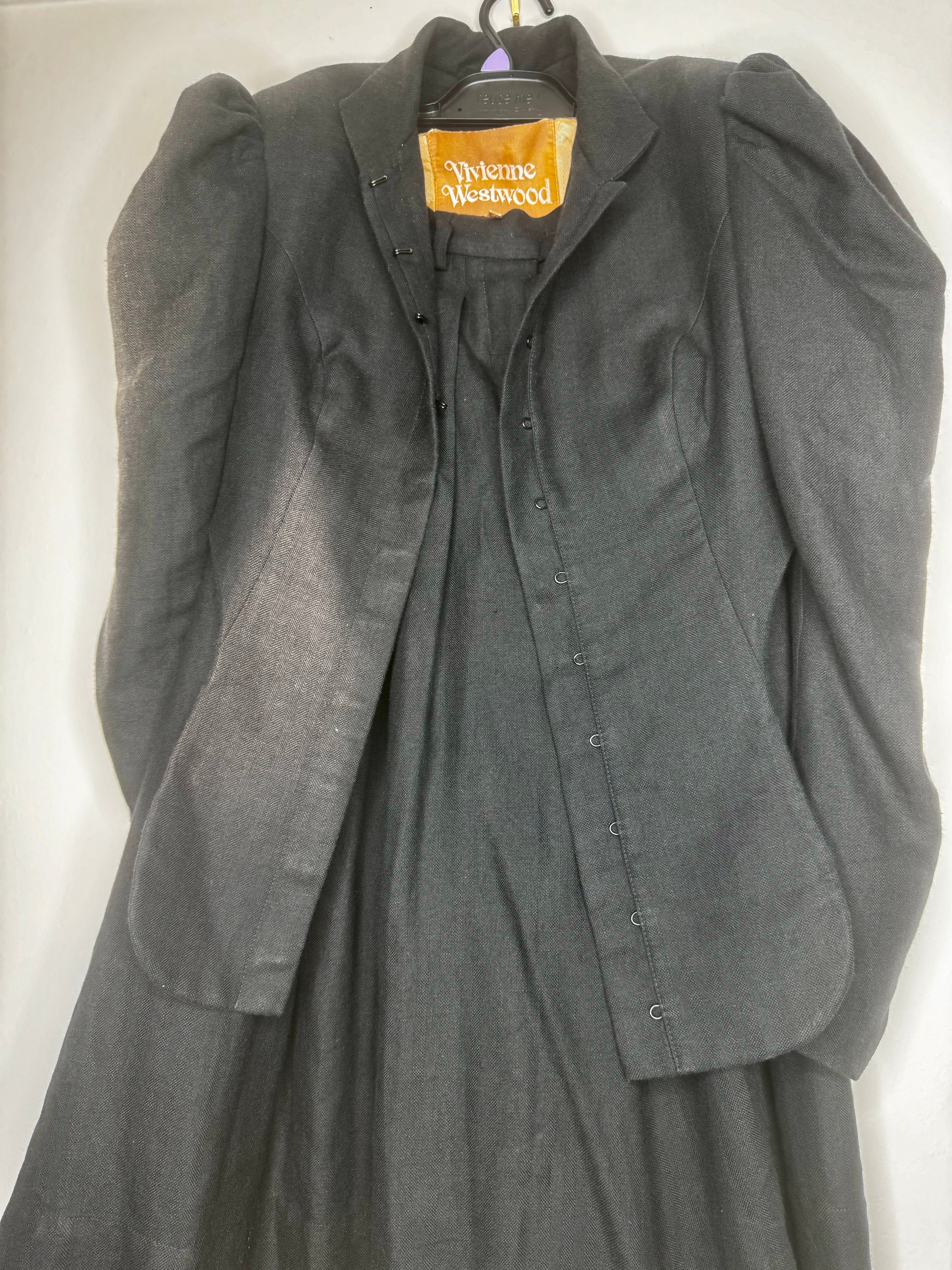 Front view of Vivienne Westwood vintage black cropped jacket and matching culotte set on hanger, showing structured tailoring and gold label lining.